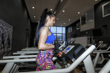 Mid adult woman running on treadmill in gym - GGGF00832