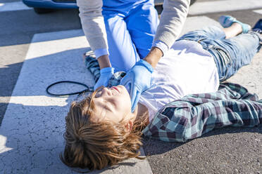 Doctor checking unconscious boy lying on road after car accident - GGGF00858