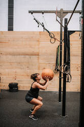 Seitenansicht einer starken schwangeren Athletin, die mit einem Medizinball in einem modernen Fitnesscenter trainiert - ADSF19979