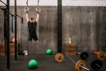 Full body strong sportswoman hanging on gymnastic rings and swinging while  exercising during intense training in dark gym stock photo