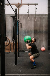 Side view of strong male athlete exercising with medicine ball in modern fitness center - ADSF19983