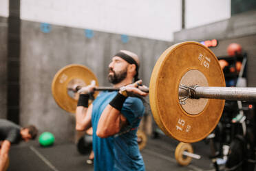 Side view of muscular male athlete doing clean and jerk exercise while training in modern fitness center - ADSF19984