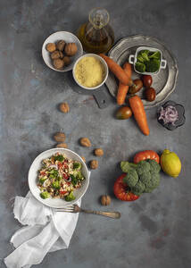 Draufsicht auf eine Schüssel mit gesundem, hausgemachtem Bulgur-Couscous-Salat mit verschiedenen Gemüsesorten und Walnüssen, serviert auf einem Tisch mit Zutaten - ADSF20001