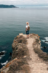 Unrecognizable male traveler standing on rocky hill and observing wonderful scenery of sea under cloudy sky - ADSF20042