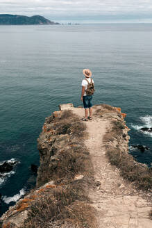 Unbekannter männlicher Reisender, der auf einem felsigen Hügel steht und die wunderbare Szenerie des Meeres unter bewölktem Himmel betrachtet - ADSF20042