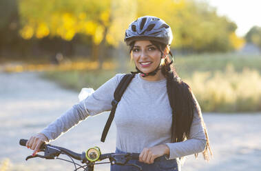 Ganzkörperaufnahme einer jungen Frau in Sportkleidung und Helm, die mit dem Fahrrad durch einen Herbstwald mit goldenem Laub an einem sonnigen Tag auf dem Land fährt - ADSF20077