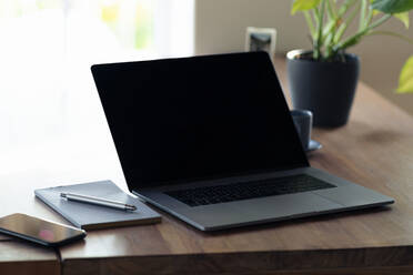 Laptop and smart phone by book on table at home office - SBOF02366