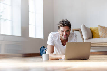 Man smiling while working on laptop at home - SBOF02370