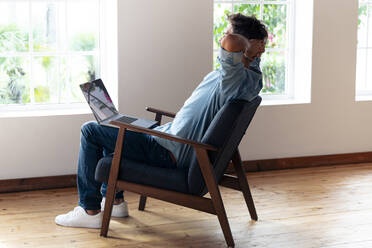 Man with hands behind head resting while sitting on armchair at home - SBOF02374