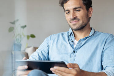 Mann benutzt digitales Tablet, während er zu Hause sitzt - SBOF02379