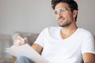 Thoughtful man with paper looking away while sitting at home - SBOF02384