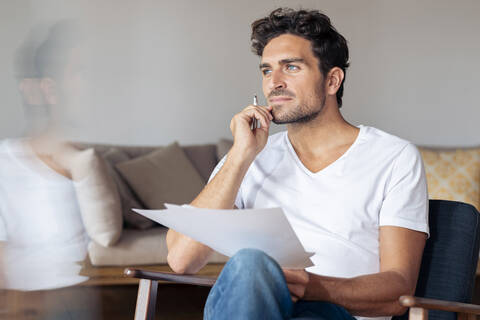 Thoughtful man with hand on chin while sitting at home stock photo