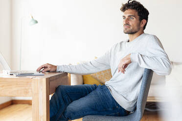 Man looking away while sitting by table at home office - SBOF02416