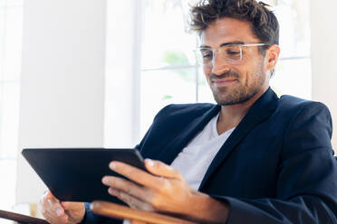 Smiling businessman using digital tablet while sitting at home - SBOF02431