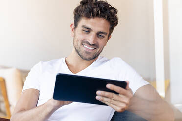 Mittelgroßer erwachsener Mann, der zu Hause sitzend ein digitales Tablet benutzt - SBOF02440