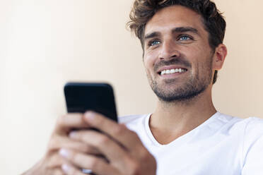 Handsome man smiling while using smart phone at home - SBOF02442
