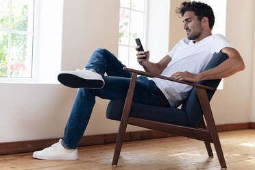 Mid adult man using smart phone while sitting armchair at home - SBOF02446