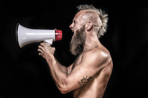 Angry male viking screaming while holding megaphone against black background stock photo