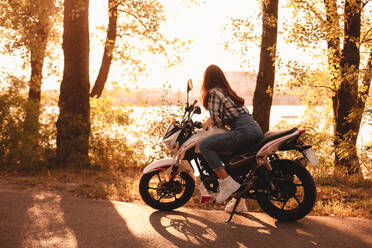 Woman looking at view while sitting on motorcycle by river - CAVF91688