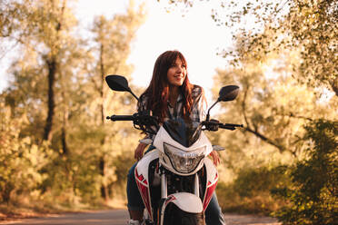 Lächelnde, selbstbewusste junge Frau auf einem Motorrad auf einer Landstraße sitzend - CAVF91693