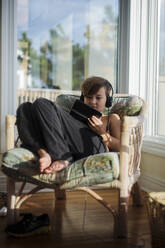 Young boy sits in a chair playing with an electronic device - CAVF91728