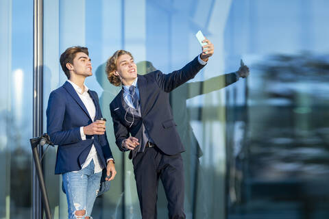 Smiling male professional taking selfie with coworker by glass on sunny day stock photo