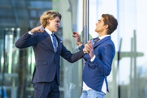 Wütender junger Geschäftsmann streitet mit einem männlichen Kollegen vor einem Bürogebäude - GGGF00878
