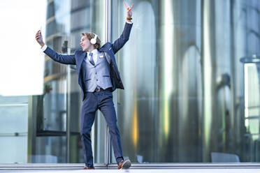 Männlicher Unternehmer tanzt beim Selfie machen und Musik hören gegen Bürogebäude - GGGF00891