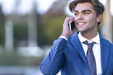 Lächelnder junger Geschäftsmann, der mit einem Mobiltelefon kommuniziert - GGGF00896