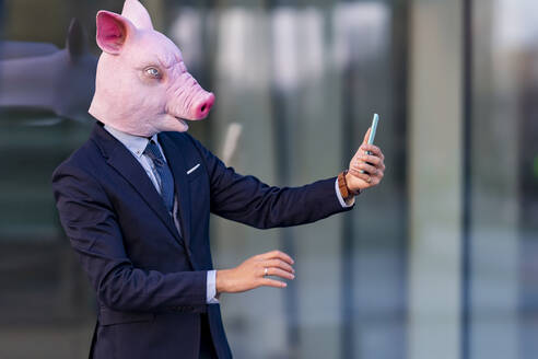 Male entrepreneur wearing pig mask on video call through smart phone - GGGF00900