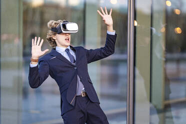 Männlicher Fachmann, der sich an einem Virtual-Reality-Simulator vor einer Glaswand amüsiert - GGGF00916