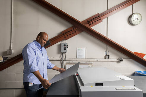 Supervisor examining paper while standing by print machine in shop - ISPF00029