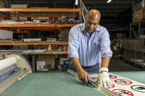 Male supervisor cutting paper signs on workbench - ISPF00037