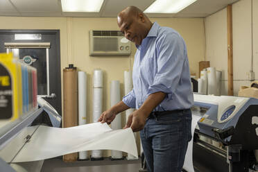 Lächelnde Aufsichtsperson, die Papier in die Druckmaschine einlegt, während sie im Geschäft arbeitet - ISPF00041