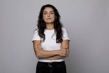 Confident woman standing with arms crossed against gray background - FLLF00557