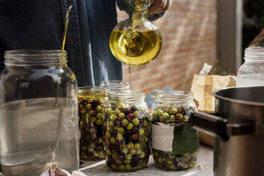 Älterer Mann gießt Olivenöl in Glasgefäß auf Tisch - AFVF08053