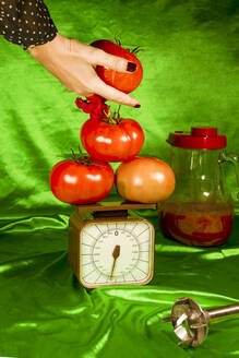 Frau wiegt Tomaten auf einer Waage vor grünem Stoff - ERRF04889