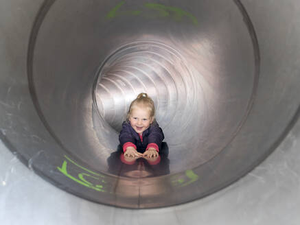 Lächelndes Mädchen, das in der Röhre rutscht und auf den Spielplatz schaut - LAF02634