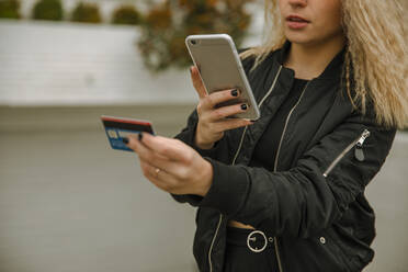 Blond woman doing online shopping through smart phone while paying through credit card - ACPF01034