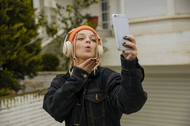 Fashionable woman blowing kiss while taking selfie through mobile phone - ACPF01041