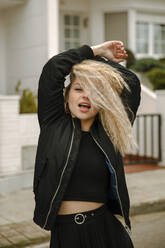 Blond hipster woman with arms raised standing on street - ACPF01049