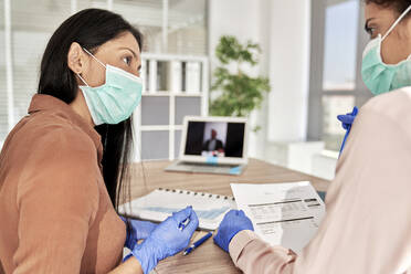 Female professionals in meeting discussing over document at work place during COVID-19 - ABIF01321