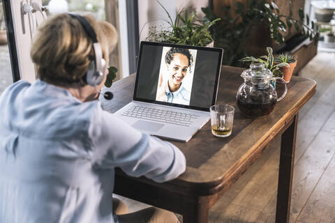 Senior woman having video call with granddaughter through laptop on table in living room stock photo