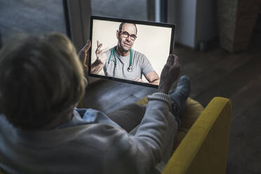 Senior patient taking advice from male doctor on video call while sitting in dark room - UUF22663