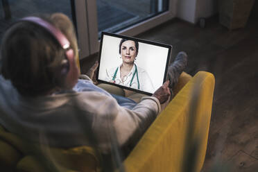 Senior woman on video call with female doctor through digital tablet in dark room - UUF22664