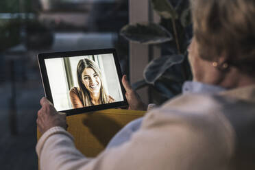 Senior woman on video call with granddaughter through digital tablet at home - UUF22665