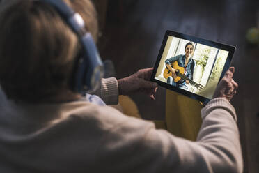 Young woman playing guitar for senior woman on video call through digital tablet at home - UUF22666