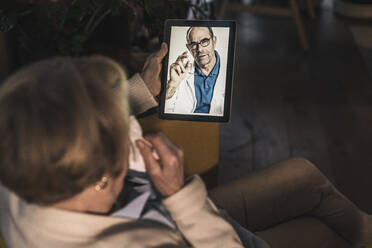 Senior patient on video call with male doctor through digital tablet at home - UUF22669