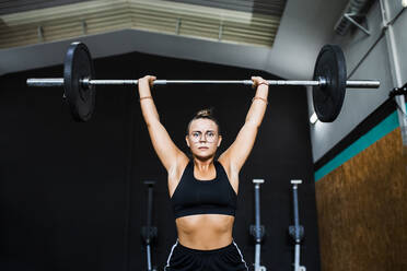 Confident female athlete lifting deadlift in gym - MIMFF00414