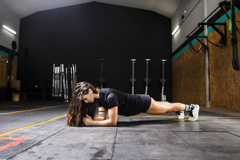 Junge Frau übt die Plank-Position auf dem Boden im Fitnessstudio - MIMFF00416